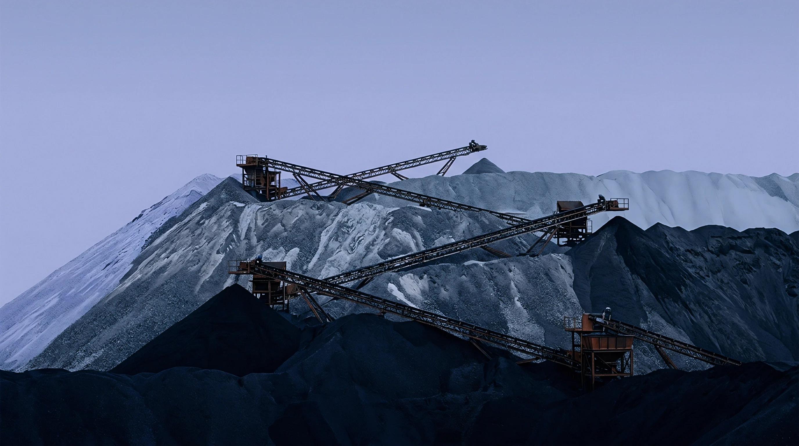 Heavy industrial conveyor structures span across massive stockpiles of dark extracted ore and white mineral aggregate under an open sky.